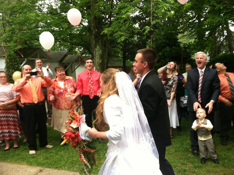 a bride and groom walk through a crowd of smiling happy wedding guests