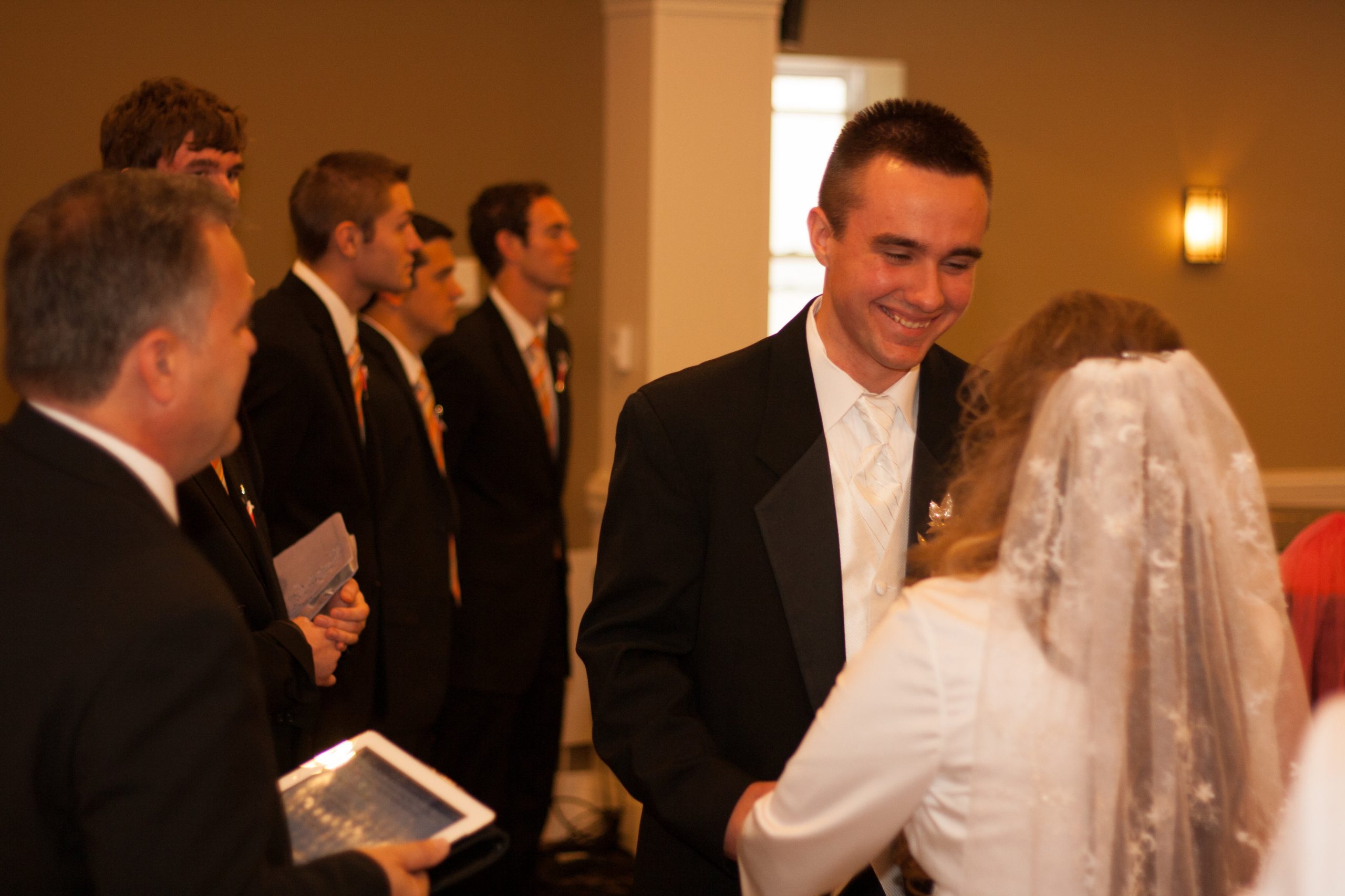 a groom smiles at his bride and a preacher stands beside them with a bible